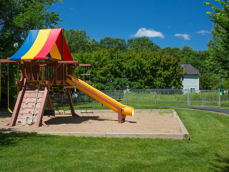 children's outdoor playground with swings, climbing wall, slide, and rainbow canopy, on a sunny day